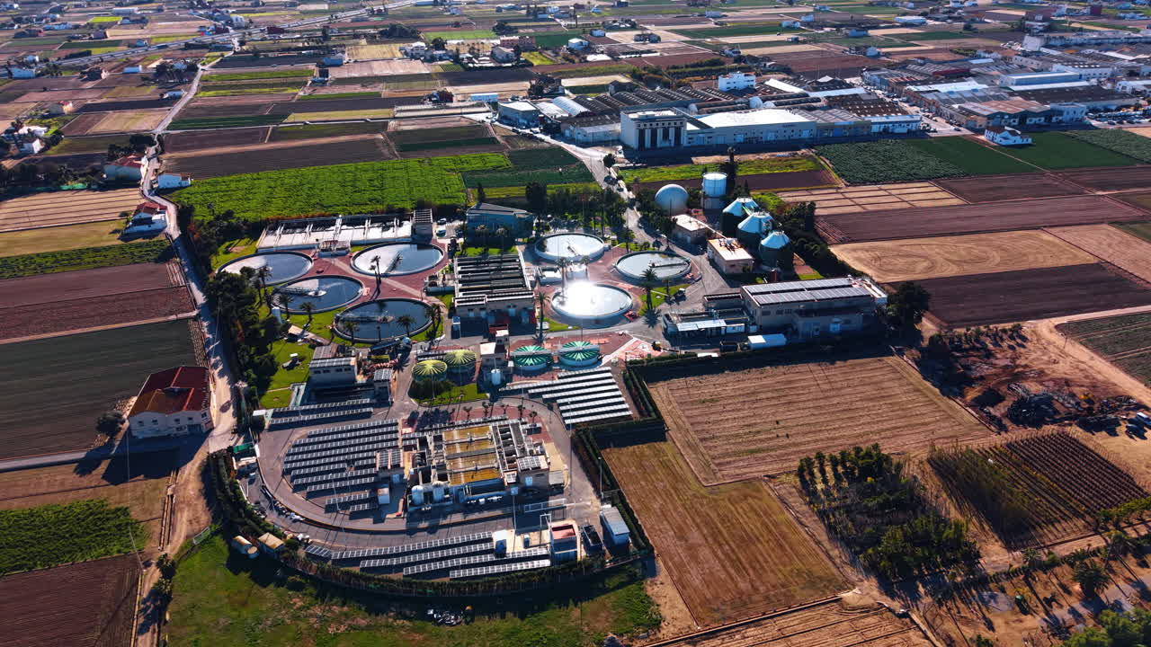 Aerial view of modern wastewater treatment plant with solar panels. Wide aerial shot of an industrial sewage treatment facility surrounded by green agricultural fields in daylight