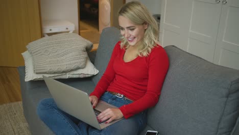 Fröhliche-Frau-Mit-Laptop-Auf-Sofa-Sitzend