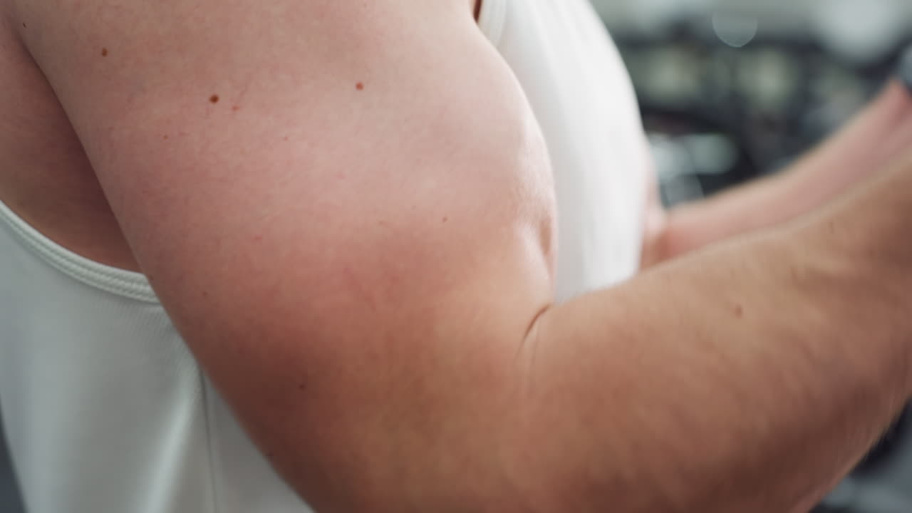 White male arm straining on cable machine handle while performing strength exercise, muscle fibers and veins visible under bright gym lighting showcasing intense training focus and power