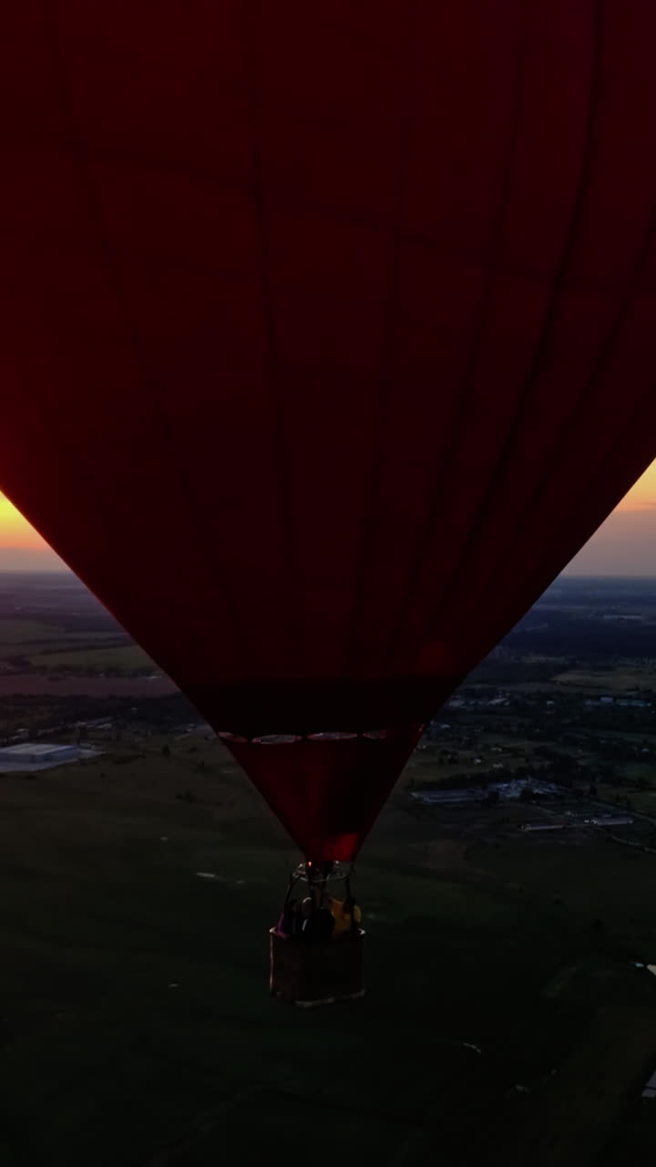 People travel in hot air balloon. Beautiful red aerostat in the form of a heart flying in the sky against orange sunset. Vertical video