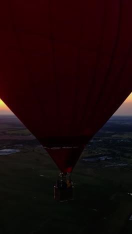 people travel in hot air balloon. beautiful red aerostat in the form of a heart flying in the sky against orange sunset. vertical video