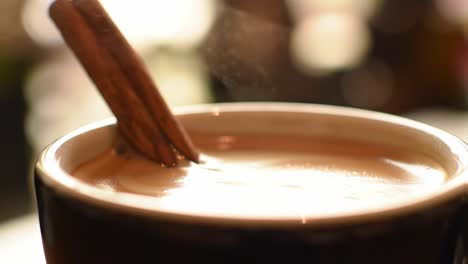 infusing flavor: a close-up view of cinnamon stirring in a steaming mug of delicious, creamy beverage, evoking comfort and warmth on a cozy day