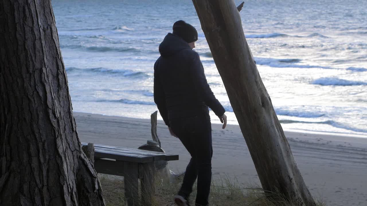북유럽 해변 숲을 탐험하는 백인 남성의 뒷모습, 해변의 회색 나무 벤치, 남자는 걷고 혼자 앉아 있고, 해안 소나무 숲, 하얀 모래 해변, 건강한 활동 개념, 중간 샷
