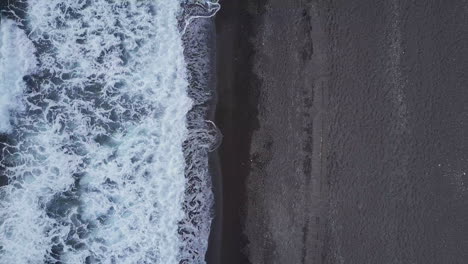 aerial looking down at waves coming in to black sand beach in mediterranean