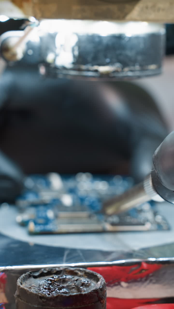 una vista de cerca de la mano de un técnico sosteniendo un soldador con humo que se eleva, indicando el proceso de soldadura, con otras herramientas a la vista