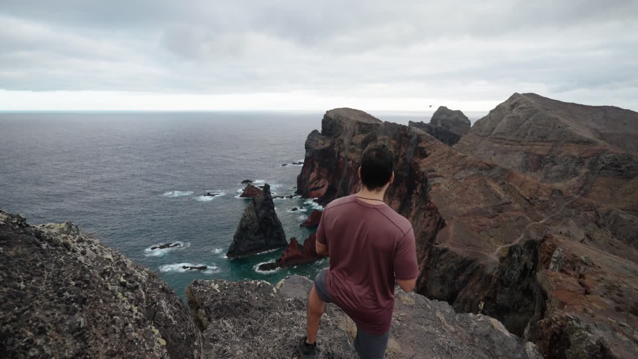 A man prepares to launch a drone while standing on a rocky cliff at Ponta de São Lourenço in Madeira, Portugal.