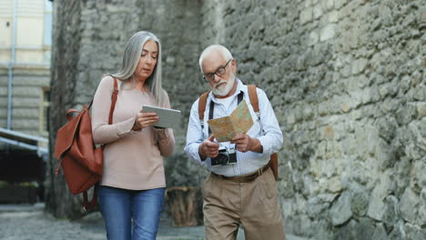 un viejo par de turistas caminando en la calle de una ciudad antigua con un mapa y una tableta