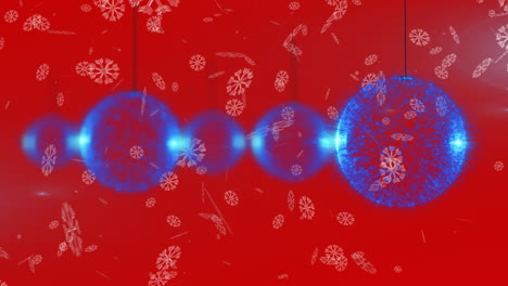 snowflakes falling over multiple blue christmas bauble hanging decorations against red background