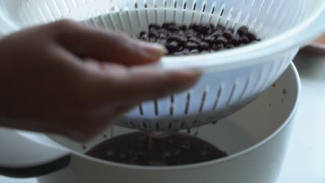 close up shot of drained black beans in a colander prepping to cook a meal two cans of beans rice plantain avocado red onion and cilantro