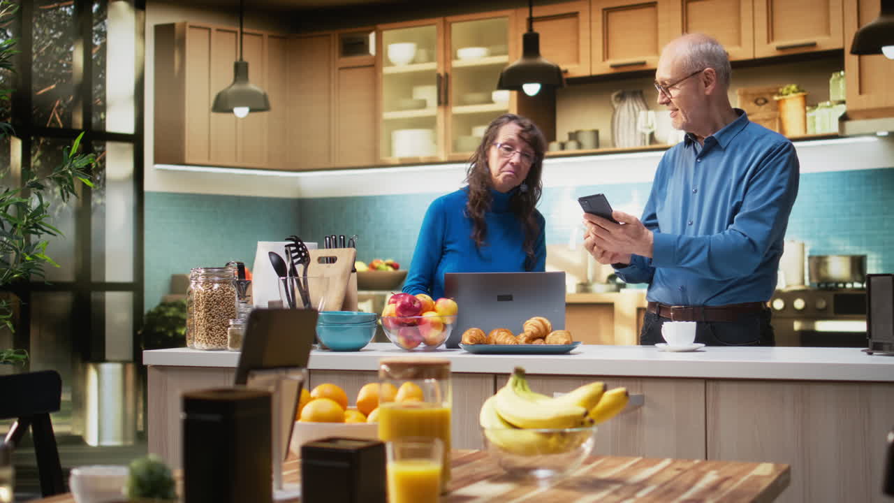 Senior couple checking smartphone apps in home kitchen with a relaxed smile
