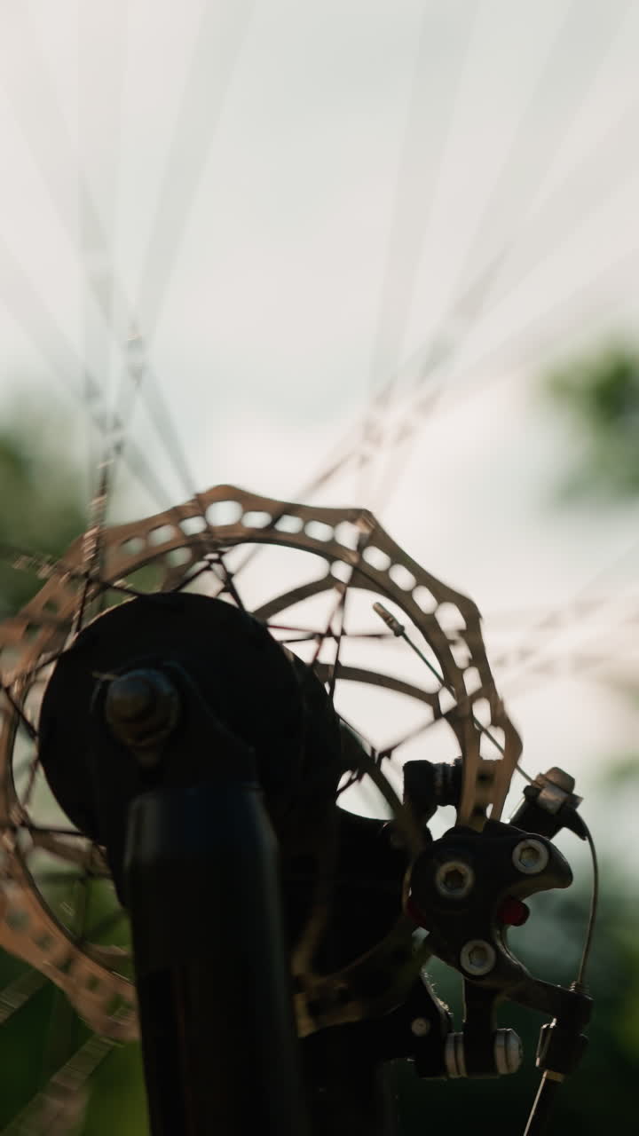 Close-up of bicycle wheel rotating both fast and slow, with sunlight reflecting off the metal components, creating a beautiful, dynamic effect while the background remains blurred