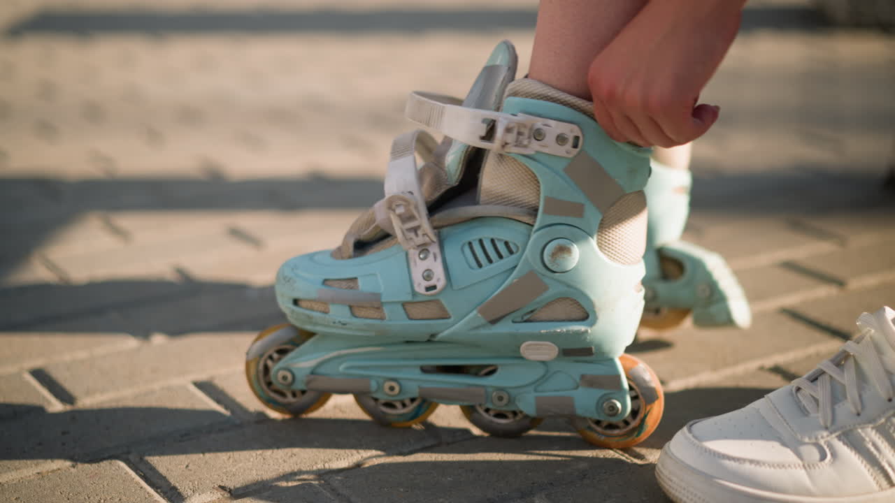Side view of individual adjusting strap on roller skate of right leg with black wristband under bright sunlight, white sneakers partially in view, background softly blurred