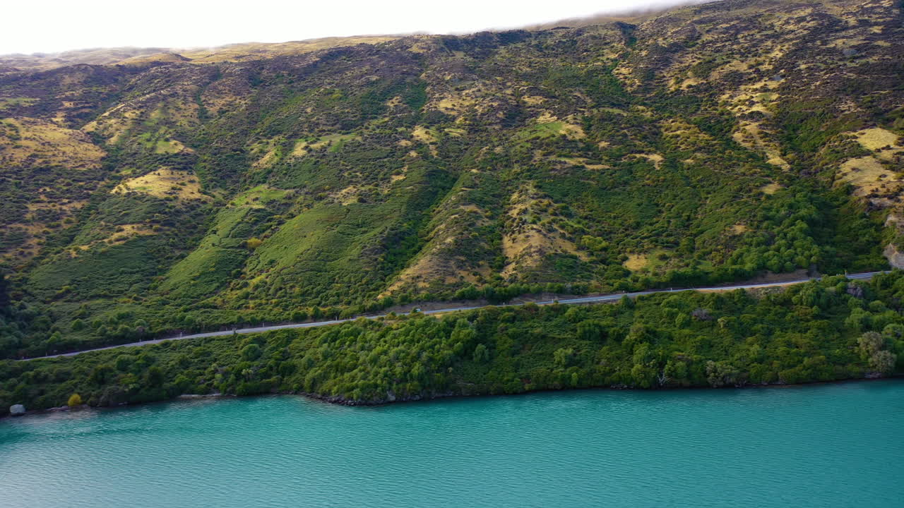 Aerial view of a scenic road along a turquoise mountain lake in the wilderness of New Zealand's Southern Alps