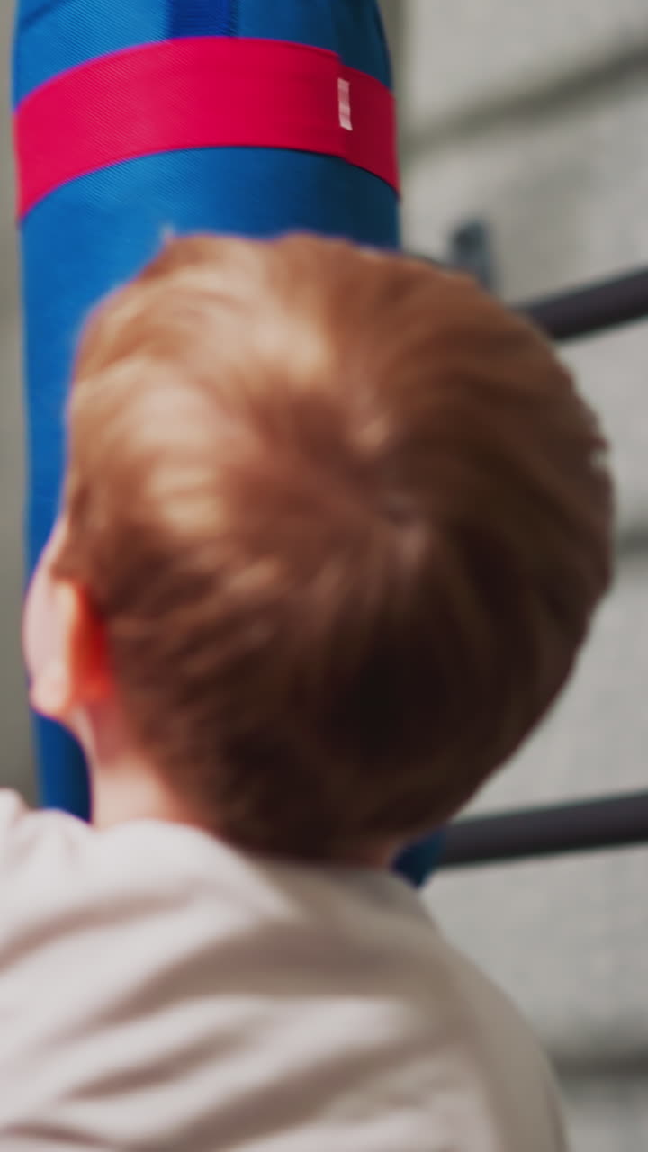 Little boy with boxing gloves punches drawing angry man on heavy bag in playing room closeup. Child deals with stress via sports exercises at home