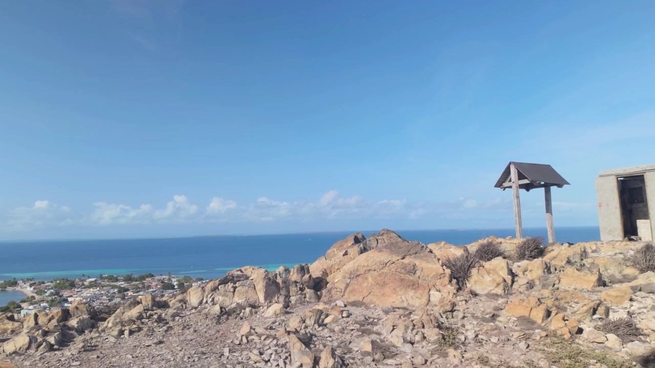 Paesaggio mozzafiato che si affaccia su una baia caraibica cristallina, con strutture di sentieri rustici e aride scogliere costiere sotto un cielo azzurro brillante.