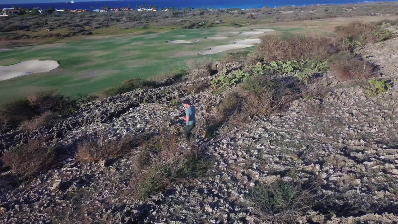 un fotógrafo de la naturaleza pisando una gran grieta en la roca volcánica, con vistas a un campo de golf en aruba
