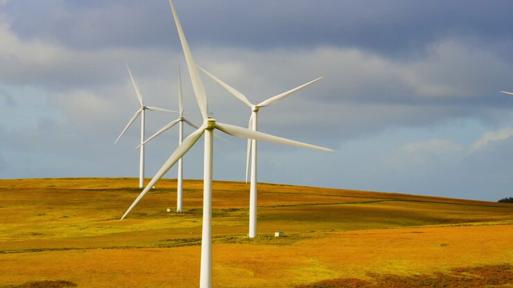 Panorering opad afslører vindmøllepark, der snurrer hurtigt rundt med fyrretræsplantage på en blæsende dag med et robust landskab. Miljøvenlig elektricitet fra vedvarende energi