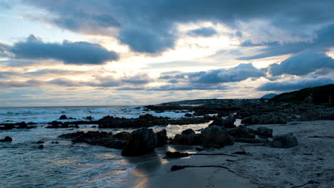 waves crash onto rocky beach during moody cloudy vibrant sunset, dolly shot