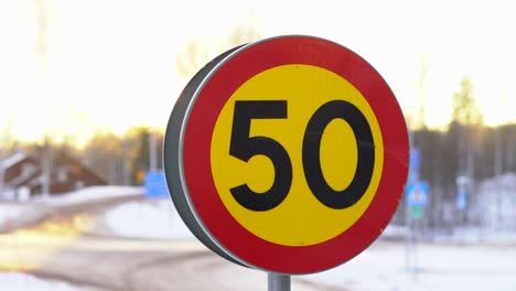 Speed limit sign with the number 50 on a snowy road during sunset in winter