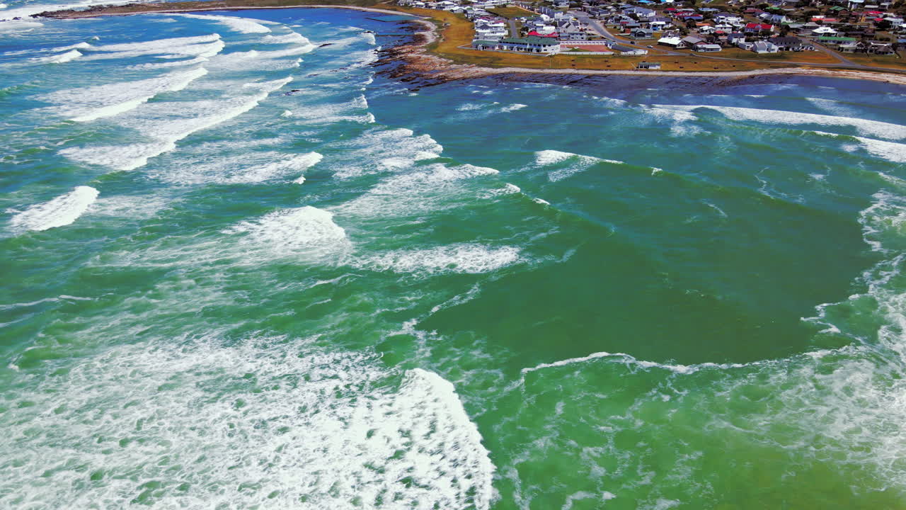 High angle drone view of L'Agulhas coastal village with waves rolling in