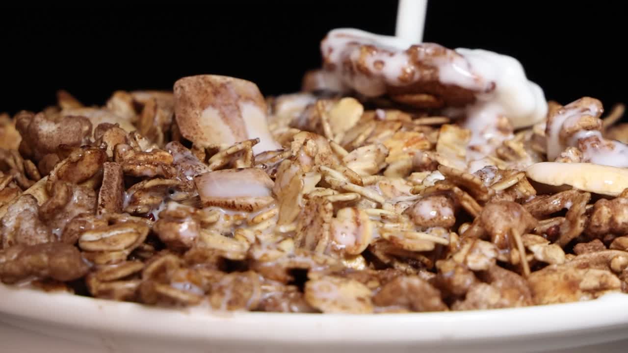 Primi piani di latte fresco che si rovescia su granola al cioccolato e colorati anelli di cereali al gusto di frutta