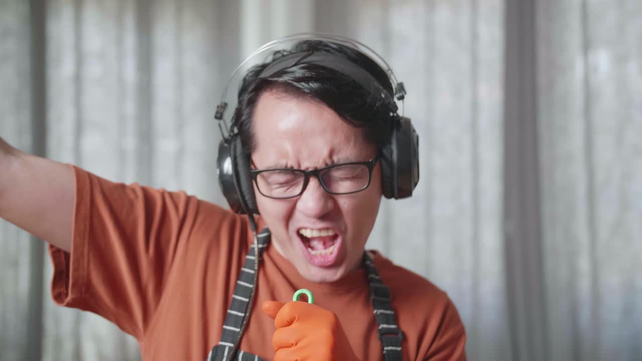 헤드폰을 착용하고 음악을 듣고 집에서 바닥을 는 동안 춤을 추는 아시안 남성 집사.