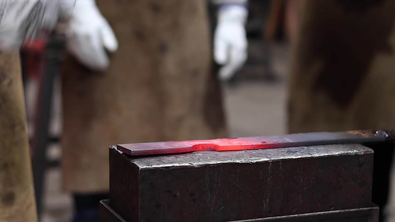 Blacksmiths forging hot metal with hammer in workshop