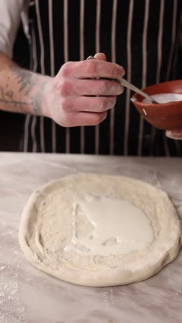 preparing a pizza with white sauce