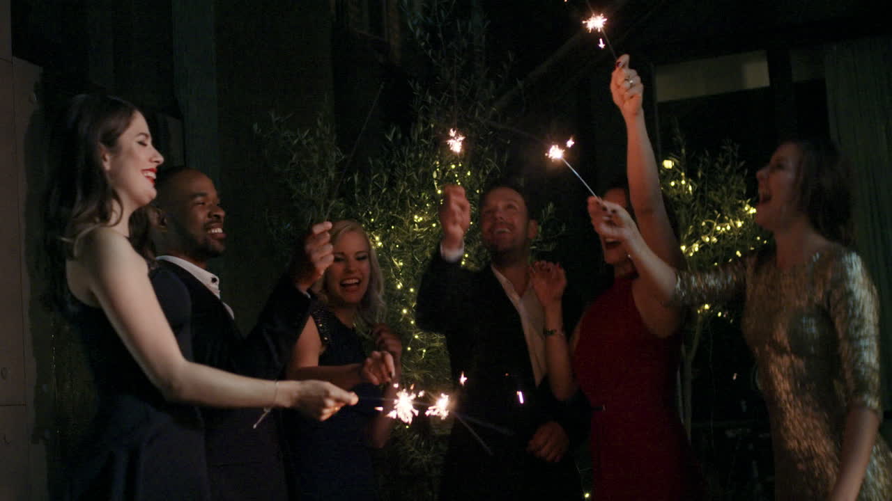 Gruppo di amici affascinanti a una festa glamour che accendono stelle filanti