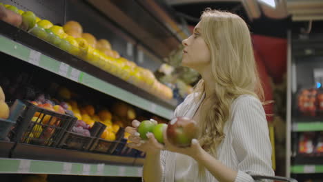 mujer joven eligiendo mangos maduros en la tienda de comestibles. chica vegana de cero residuos comprando frutas y verduras en el supermercado orgánico y usando bolsa de productos reutilizables. 4k cámara lenta