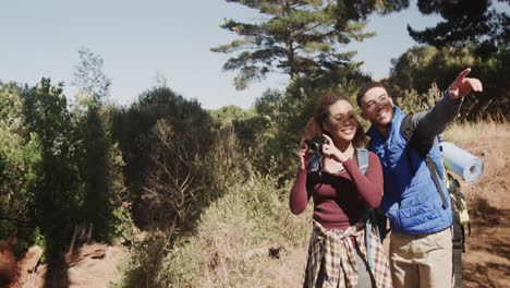 una feliz pareja afroamericana haciendo senderismo y usando mochilas, tomando fotos en el bosque, en cámara lenta