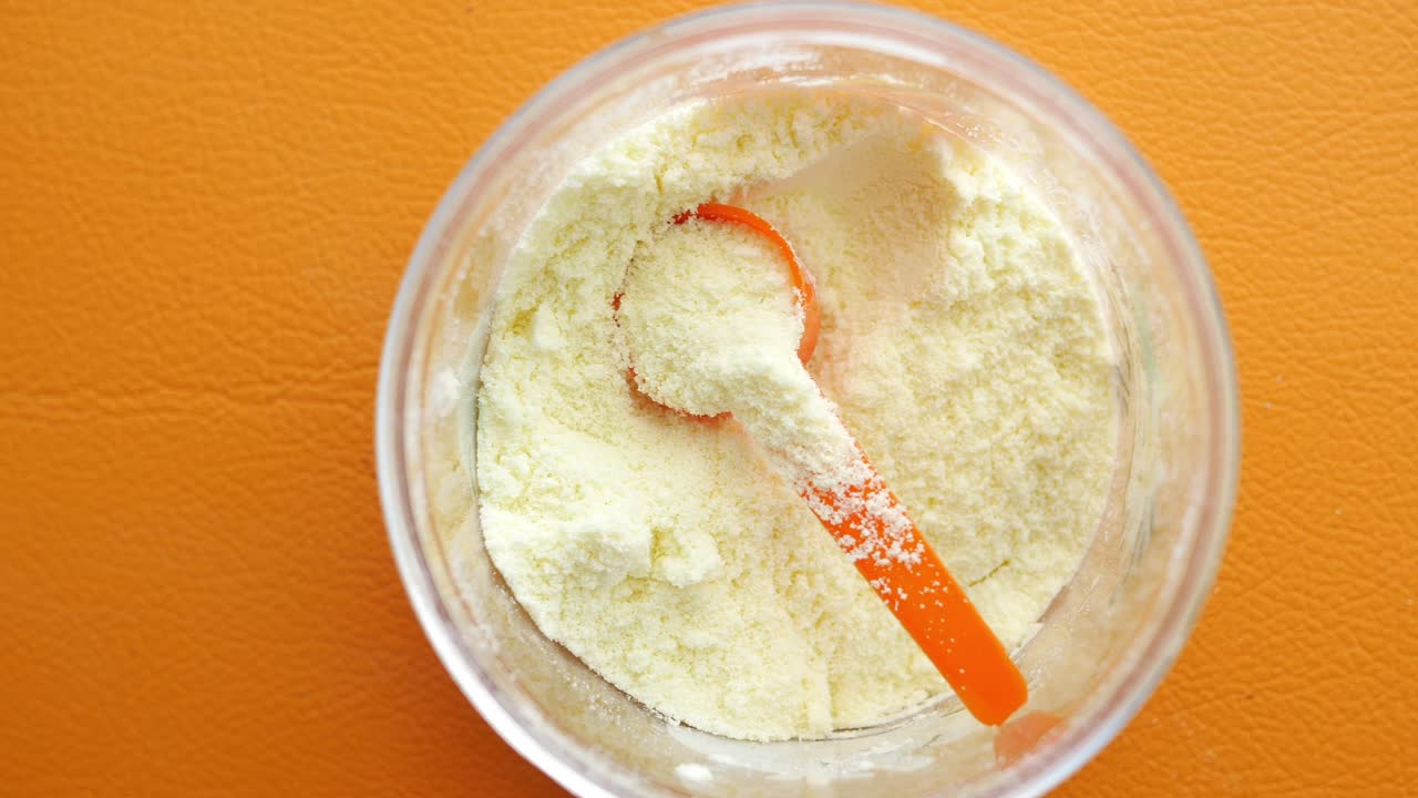 fórmula para bebés en un recipiente con cuchara medidora naranja