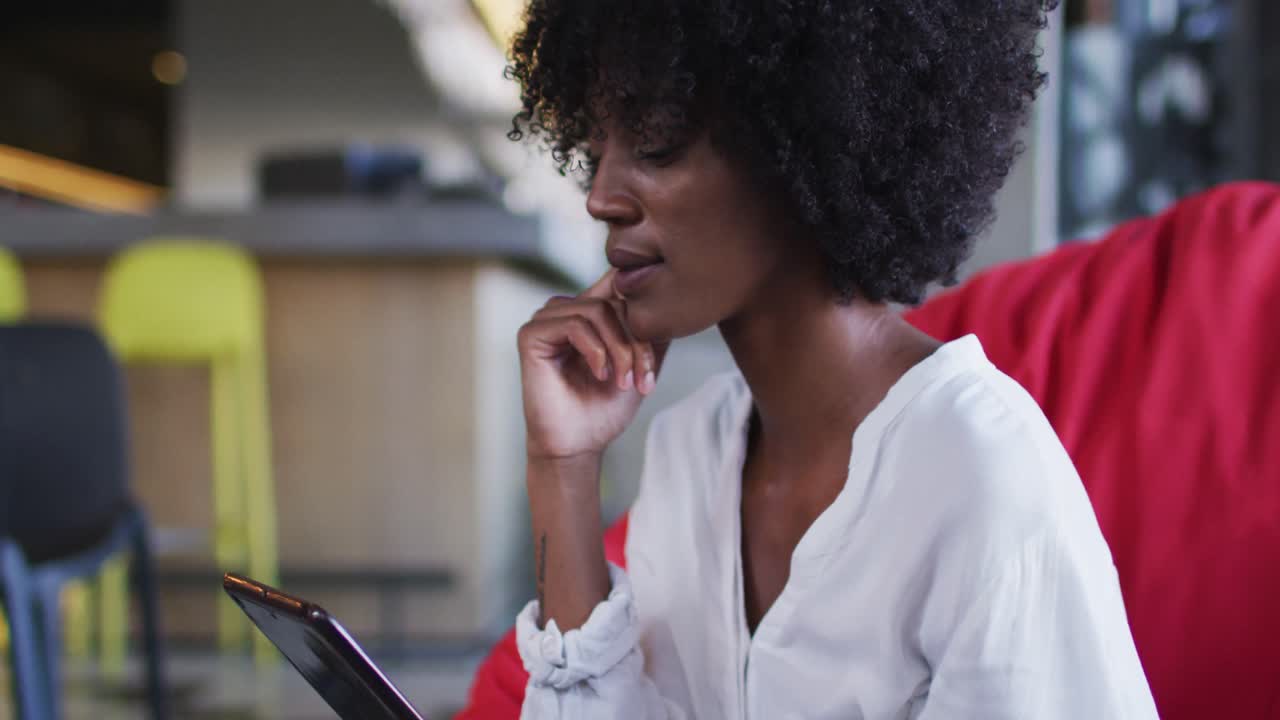 Happy african american woman sitting in cafe using digital tablet and smiling
