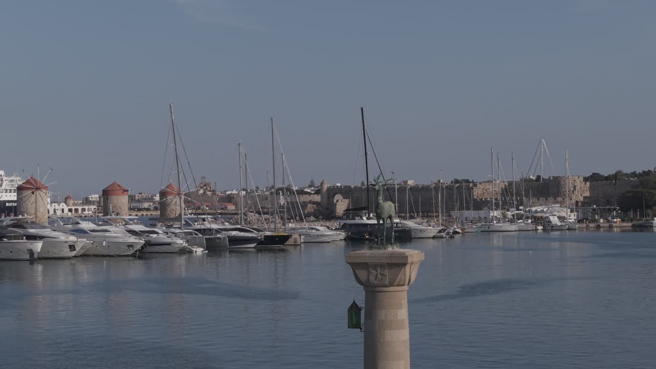 Aerial drone footage of Mandraki Harbor in Rhodes, Greece, showing the historic deer statues Captured with 3x telephoto lens. D-Log M