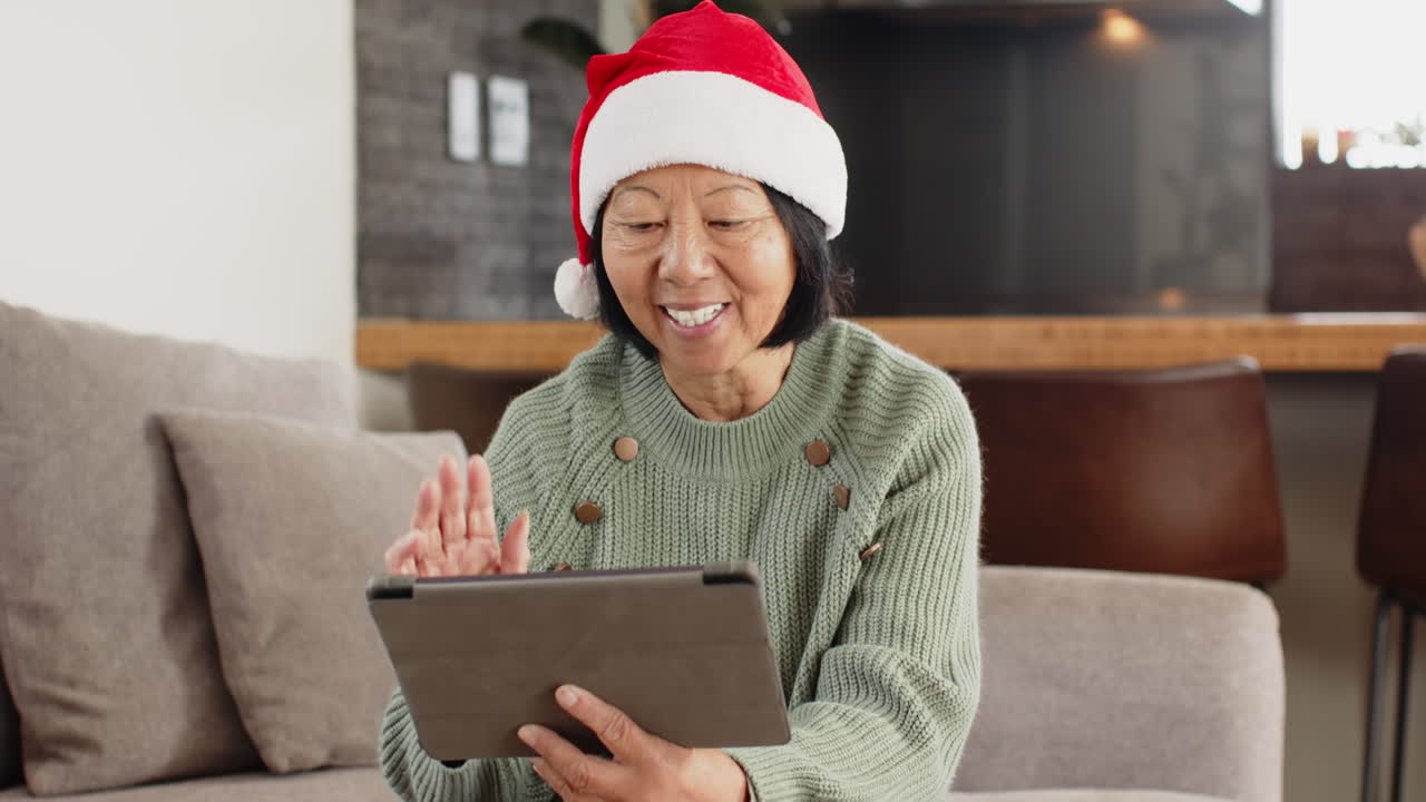 Christmas time, Senior woman wearing Santa hat video chatting on tablet at home, smiling warmly