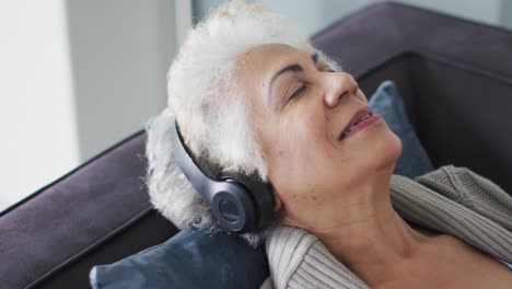 primer plano de una mujer mayor afroamericana con auriculares escuchando música sentada en el sofá