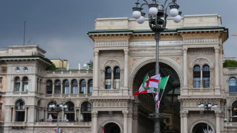 The-Famous-Galleria-Vittorio-Emanuele-in-Milan-on-a-cloudy-day-with-flags-in-front