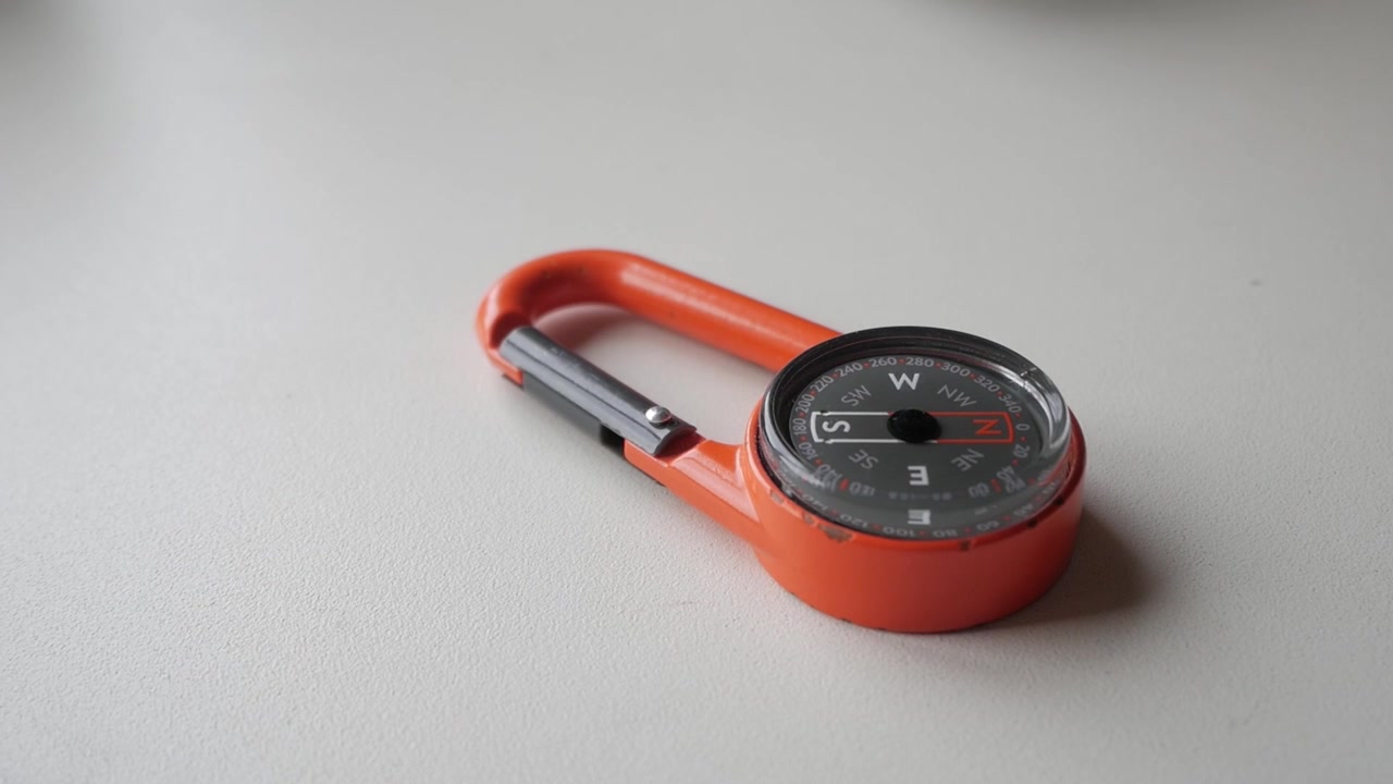 Orange compass carabiner on a surface, perfect for outdoor navigation