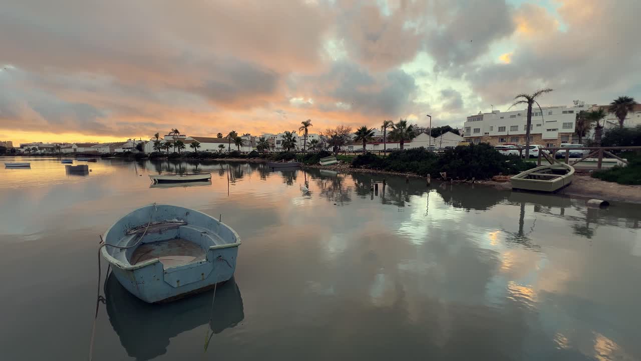 작은 시 배는 해가 지면 바바테 강에 정박하여 구름이 가득한 하늘과 스페인 안달루시아 바바테의 다채로운 도시 풍경을 반영하여 조용하고 그림 같은 풍경을 만니다.