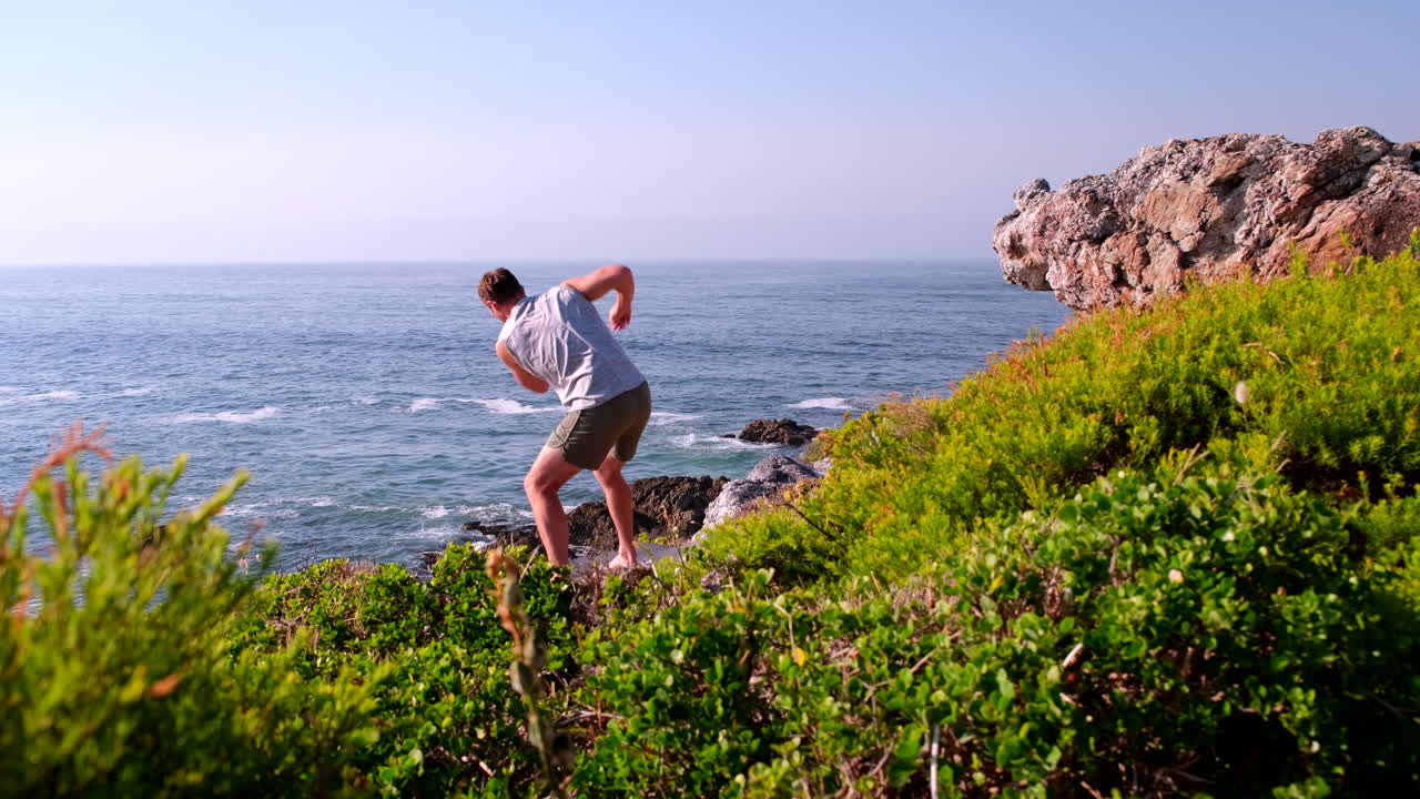Man do trunk twists in flow state for lymphatic drainage on sea cliff at sunrise