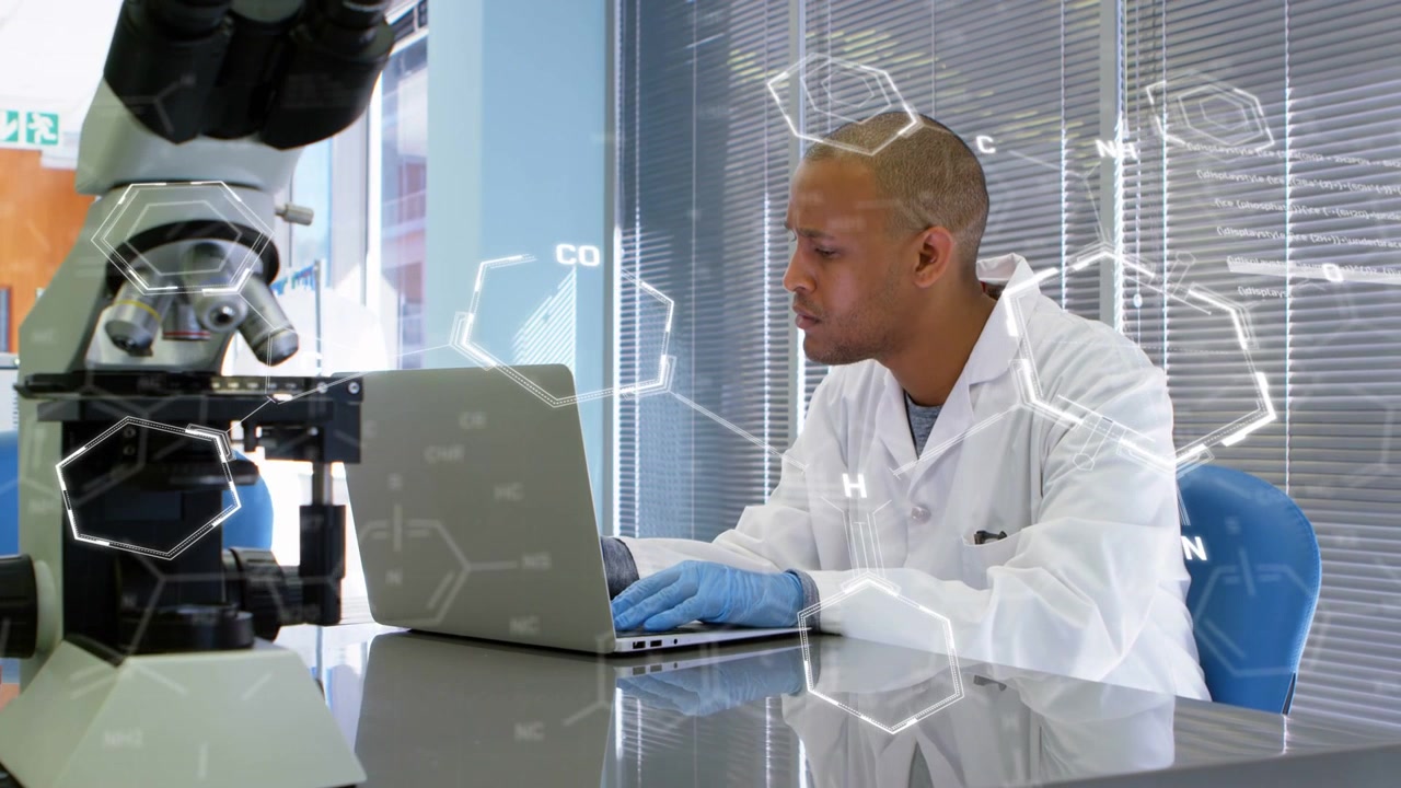 Scientist typing on laptop in lab creating molecular overlay over microscope while analyzing data