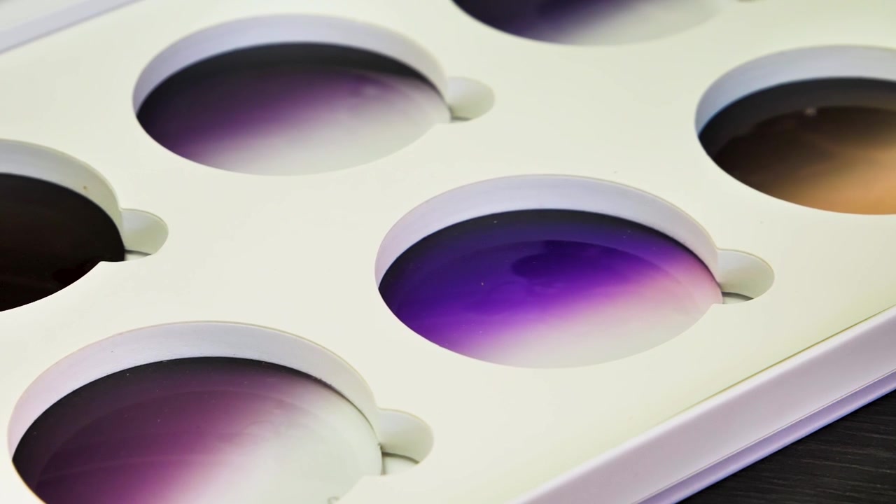Close-up of sample tinted lenses in a display case in a lens factory in Jiangsu Province, China, showcasing a variety of gradient colors and optical quality.