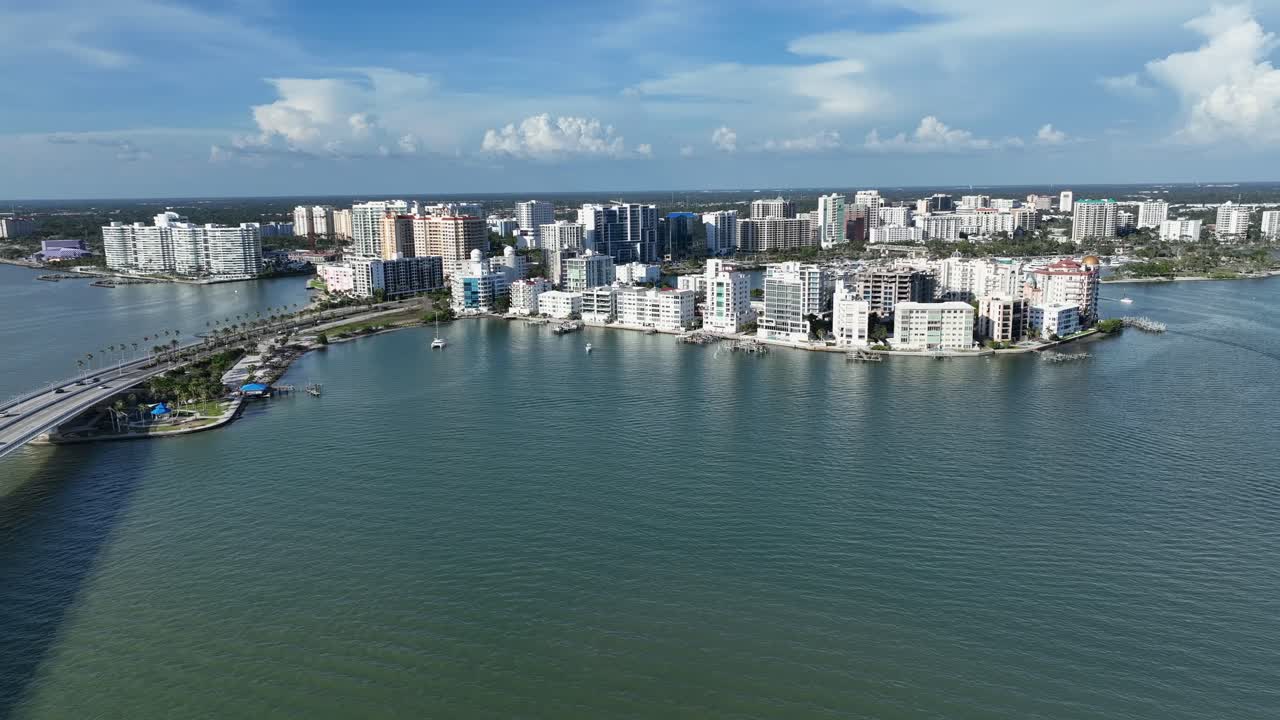 Stunning aerial view of Sarasota, Florida’s waterfront skyline. Modern beachfront condos line the coast under a bright blue sky with boats dotting the calm turquoise waters. Aerial wide shot. FL, USA