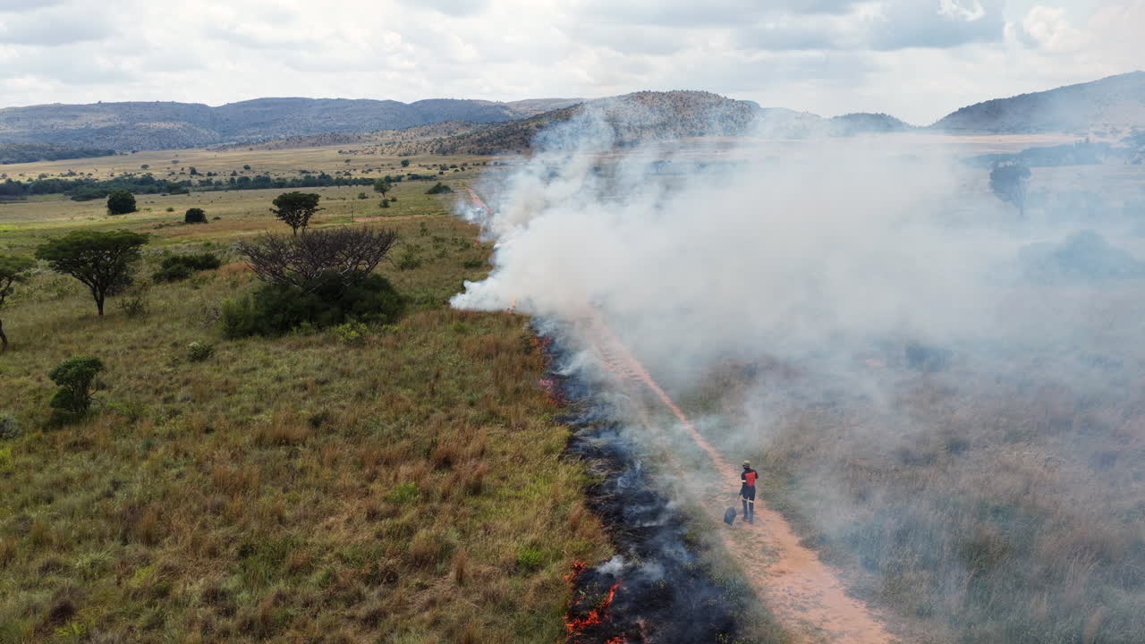 Trabalhador rural com equipamento de segurança usa um batedor de borracha para controlar uma linha de fogo, técnicas de manejo de fogo.