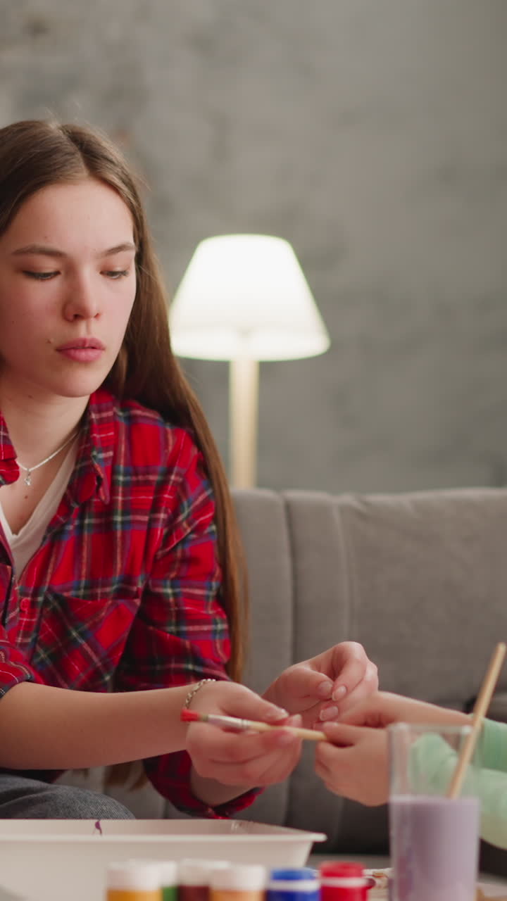 hermana adolescente enseña a una niña rubia a gotear pintura para la decoración de mármol en la sala de estar en cámara lenta. arte tradicional ebru y huevos de pascua