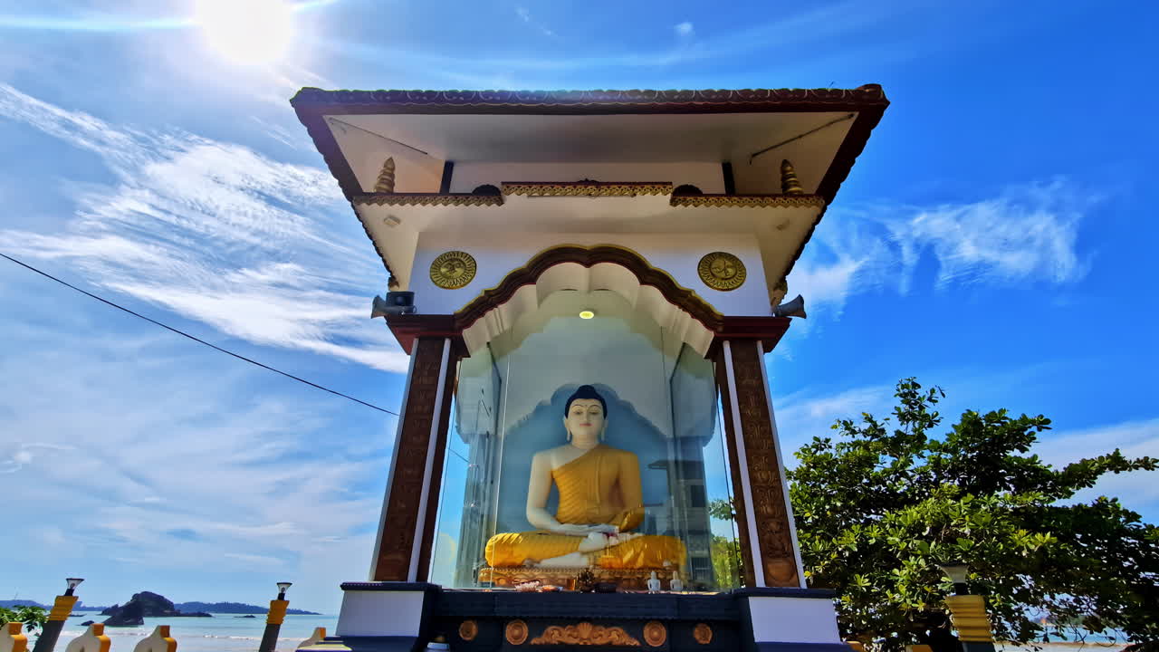 Tilt down shot revealing a serene Buddha statue in a glass shrine on the coast of Weligama a popular beach town in Sri Lanka