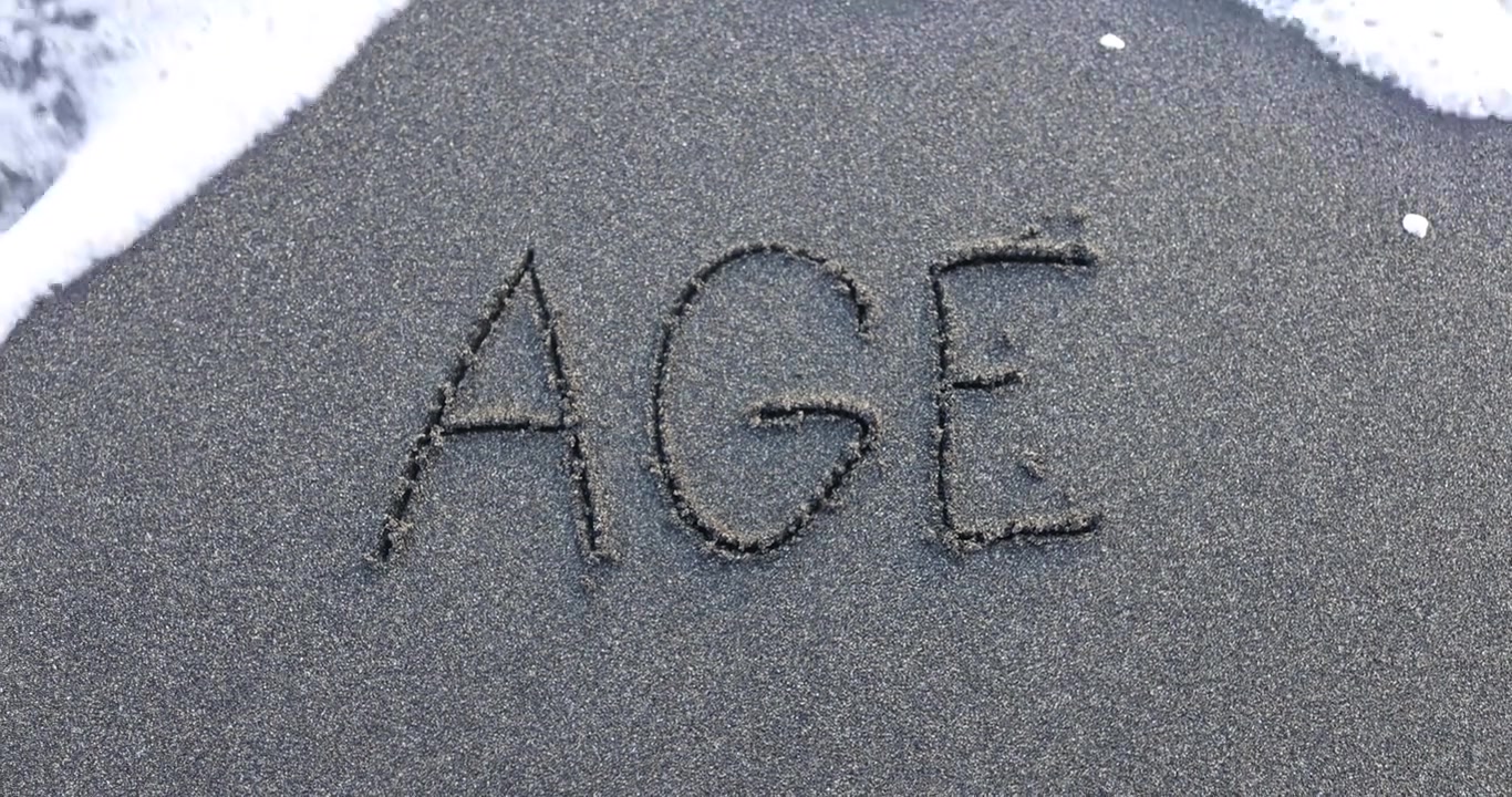 Grande parola 'age' scritta vicino alla riva nella sabbia umida della spiaggia