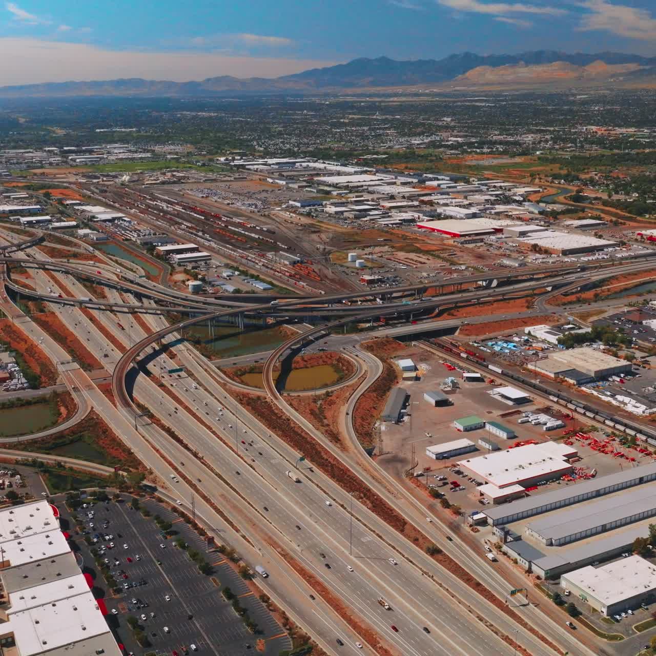 Multi-lane roads and flyovers in the industrial area. Green residential part of the city with mountains at backdrop. Salt Lake City panorama at sunny daytime