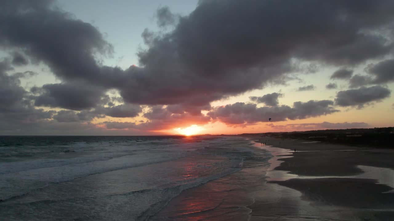 puesta de sol en la playa con nubes dramáticas que reflejan el caloroso resplandor del sol, olas que golpean suavemente la orilla