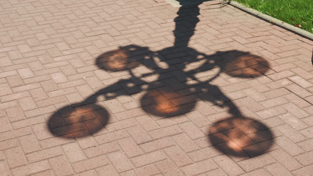 sunlit amber lamp shadow on brick pavement, vintage street fixture casts five glowing discs, warm orange reflections on textured pavers, late afternoon light, quiet urban walkway near grass verge